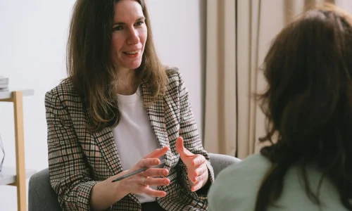pexels-photo-7176288-7176288 Pensive woman psychologist with brown hair in stylish clothes sitting and talking with unrecognizable female in light room